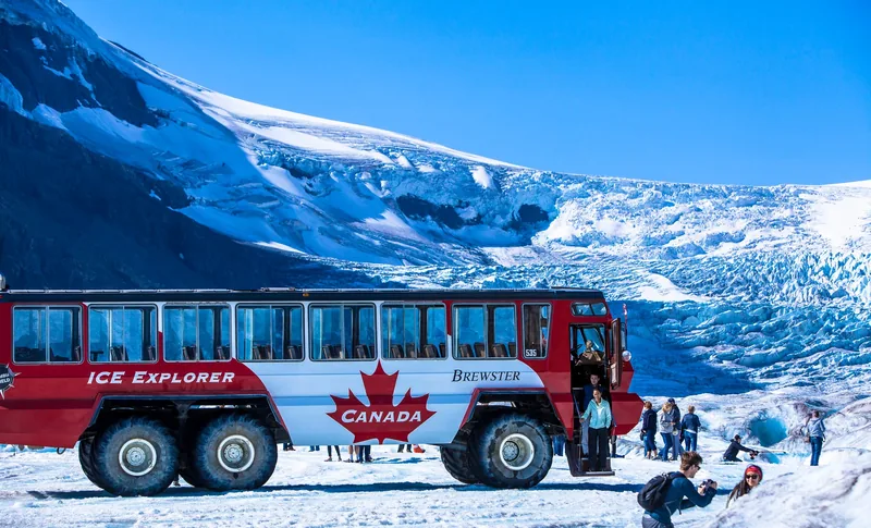 A red Ice Explorer parked on the Athabasca Glacier with visitors standing on the ice beside it