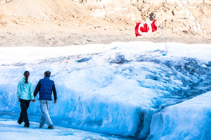 Two visitors walking on the blue ice of the Athabasca Glacier inside the roped visitor area